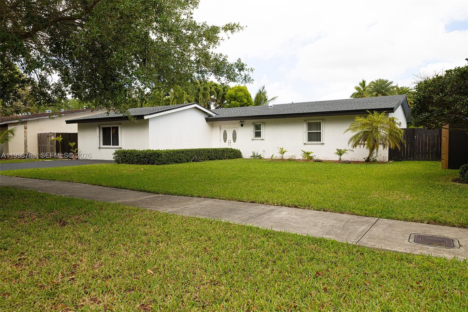 A single-story white house with a dark roof sits behind a green lawn and sidewalk — 10241 SW 128th Ave, Miami FL 33186, MIAMI, FL