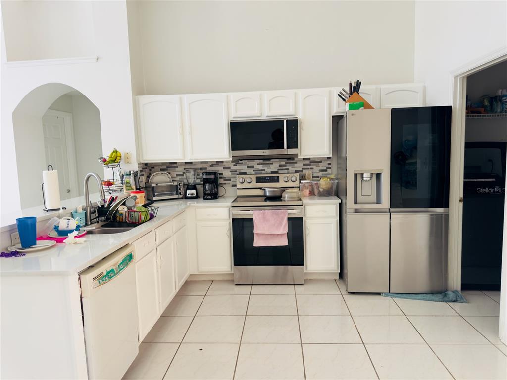 A kitchen features white cabinets, stainless steel appliances, a tiled backsplash, and white floor tiles — 4450 MALVERN HILL DRIVE, ORLANDO, FL