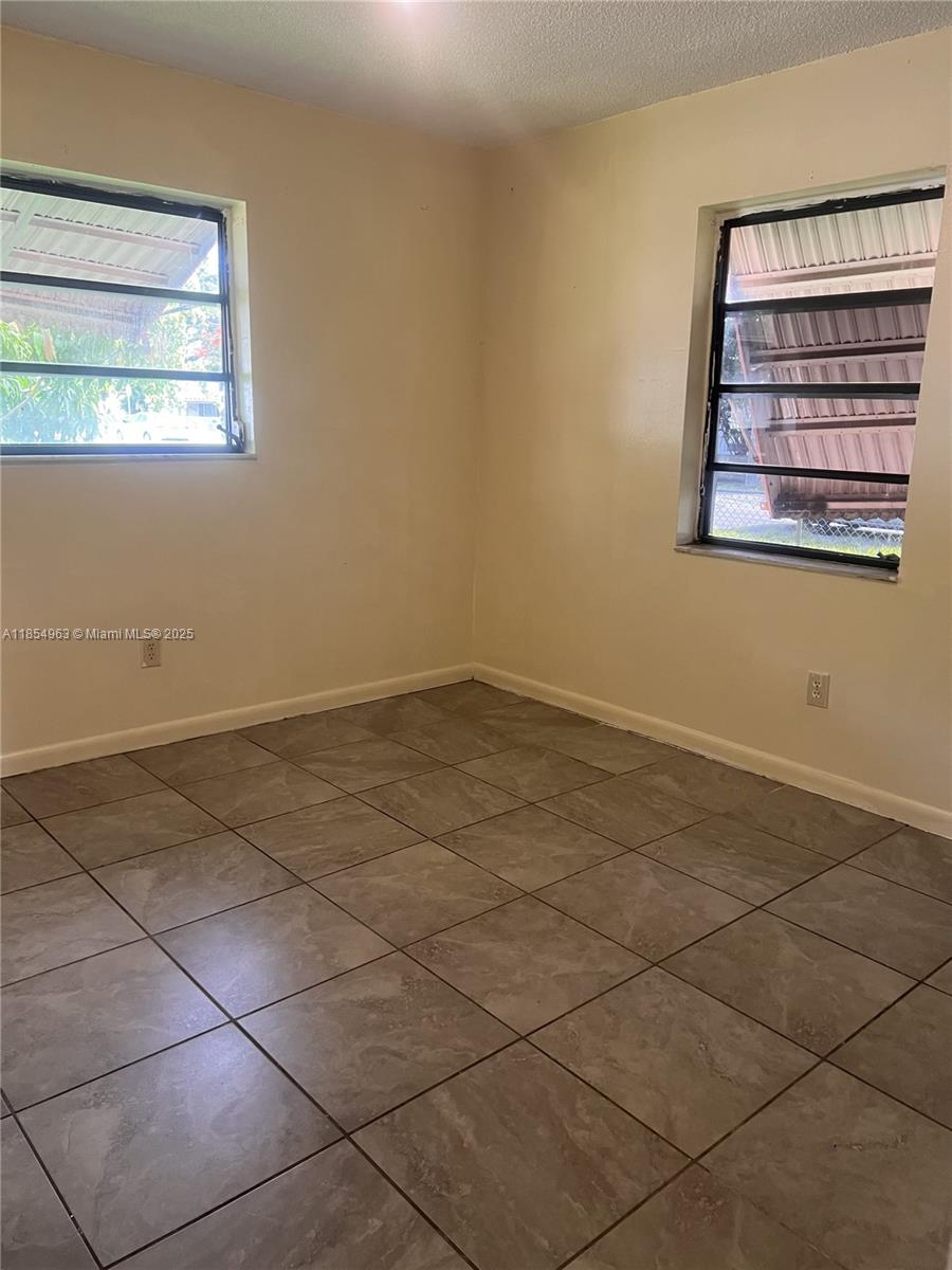An empty room features beige walls, tiled flooring, and two windows with black frames — 6150 Dawson St # 0, Hollywood FL 33023, HOLLYWOOD, FL
