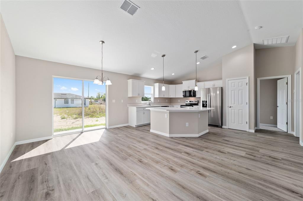 An open-concept kitchen and dining area features white cabinets, stainless appliances, and wood-look flooring — 15159 SW 29TH STREET, OCALA, FL