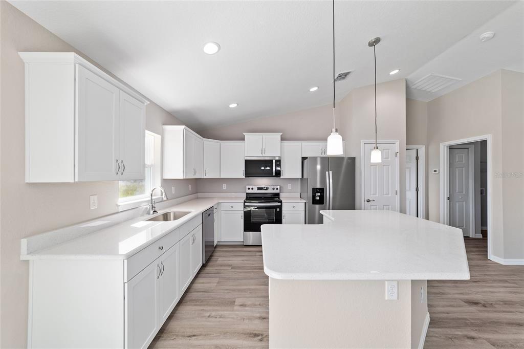 A modern kitchen features white cabinets, stainless steel appliances, and a large white island — 15159 SW 29TH STREET, OCALA, FL
