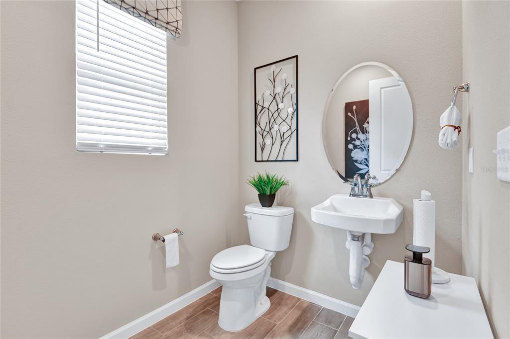 A half bathroom features a pedestal sink, oval mirror, toilet, and wood-look tile flooring — 1249 DAISY HILL AVENUE, DUNDEE, FL