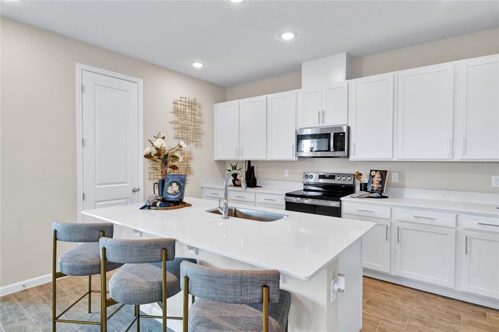 A modern kitchen features white cabinets, a central island with bar seating, and stainless appliances — 1249 DAISY HILL AVENUE, DUNDEE, FL