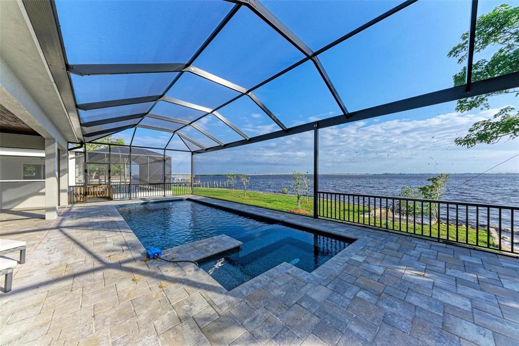 A screened-in patio features a swimming pool with an integrated spa overlooking a large lake — 116 NORTHSHORE TERRACE, PUNTA GORDA, FL