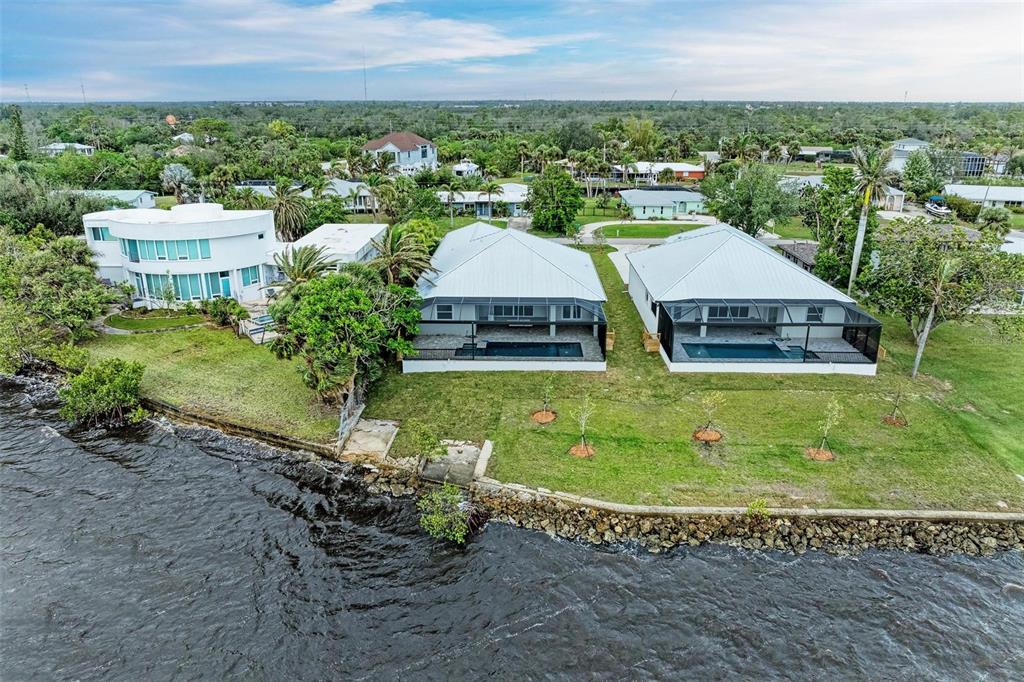 An aerial view shows three waterfront houses with pools and a stone seawall — 116 NORTHSHORE TERRACE, PUNTA GORDA, FL