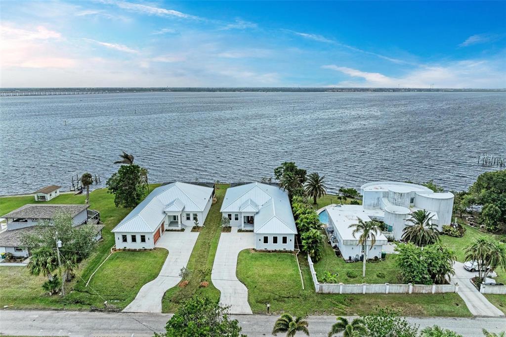 An aerial view shows three waterfront houses with white roofs and lawns along a large body — 116 NORTHSHORE TERRACE, PUNTA GORDA, FL