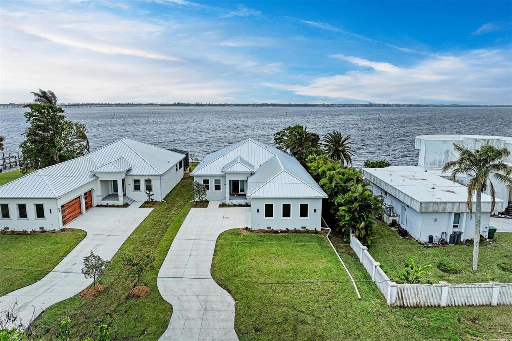 An aerial view shows two modern houses with metal roofs situated along a waterfront — 116 NORTHSHORE TERRACE, PUNTA GORDA, FL