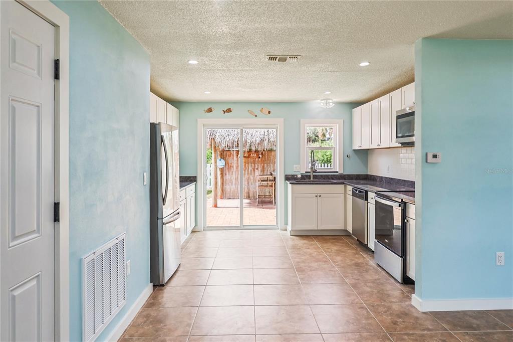 A kitchen with light blue walls, white cabinets, stainless steel appliances, and a sliding glass door — 6814 DRIFTWOOD DRIVE, HUDSON, FL