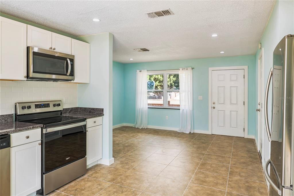 A kitchen with white cabinets, stainless steel appliances, and tile flooring opens to a dining area — 6814 DRIFTWOOD DRIVE, HUDSON, FL