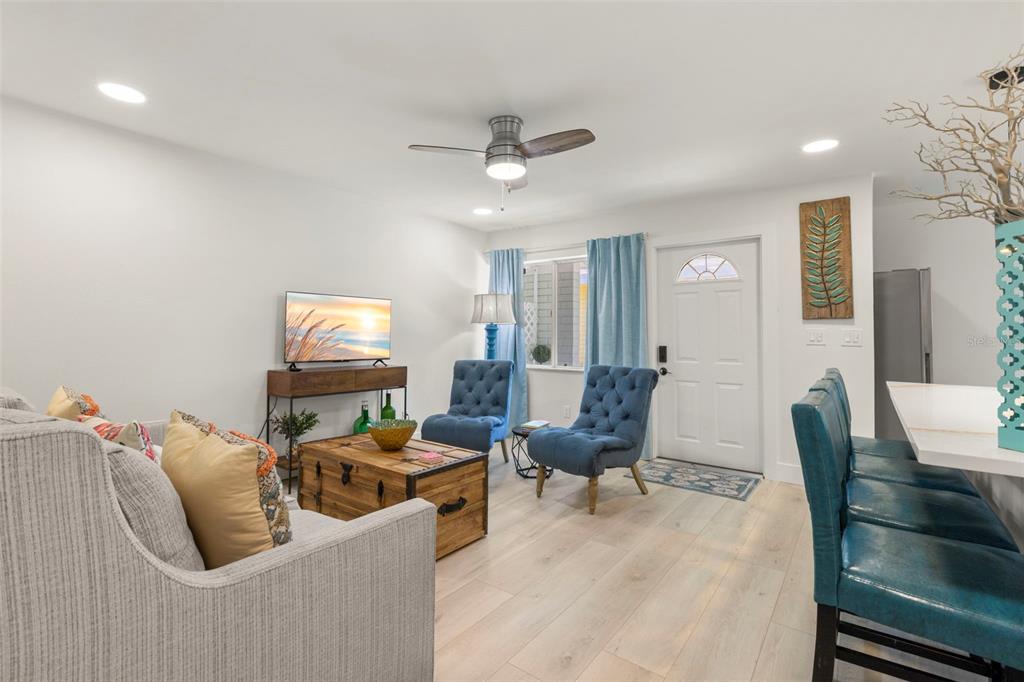 A living room features light wood flooring, a gray sofa, two blue chairs, and a television — 415 MAPLE WAY UNIT A & B, SAFETY HARBOR, FL