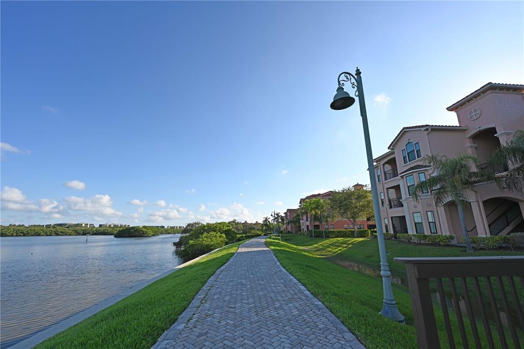 A paved walkway runs alongside a calm body of water and multi-story apartment buildings — 2755 VIA CAPRI DRIVE UNIT 1226, CLEARWATER, FL