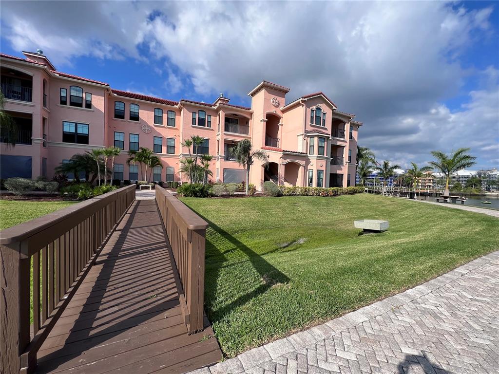 A wooden footbridge leads to a multi-story pink apartment building with a grassy lawn — 2755 VIA CAPRI DRIVE UNIT 1226, CLEARWATER, FL