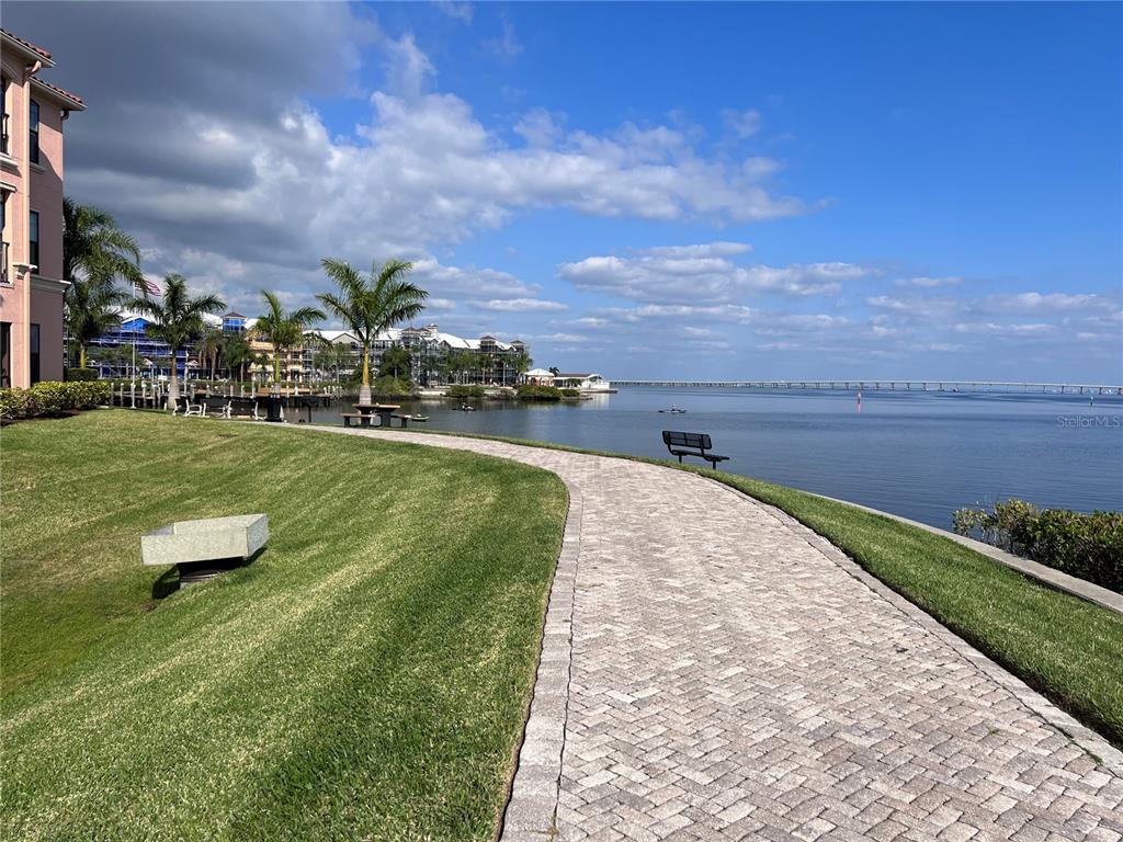 A paved walkway curves through a grassy lawn beside a bay with a distant bridge — 2755 VIA CAPRI DRIVE UNIT 1226, CLEARWATER, FL