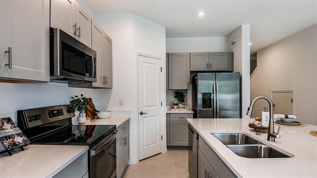 A modern kitchen features gray cabinetry, stainless steel appliances, and a white quartz island countertop — 8433 LUNAR SKYE STREET, SARASOTA, FL