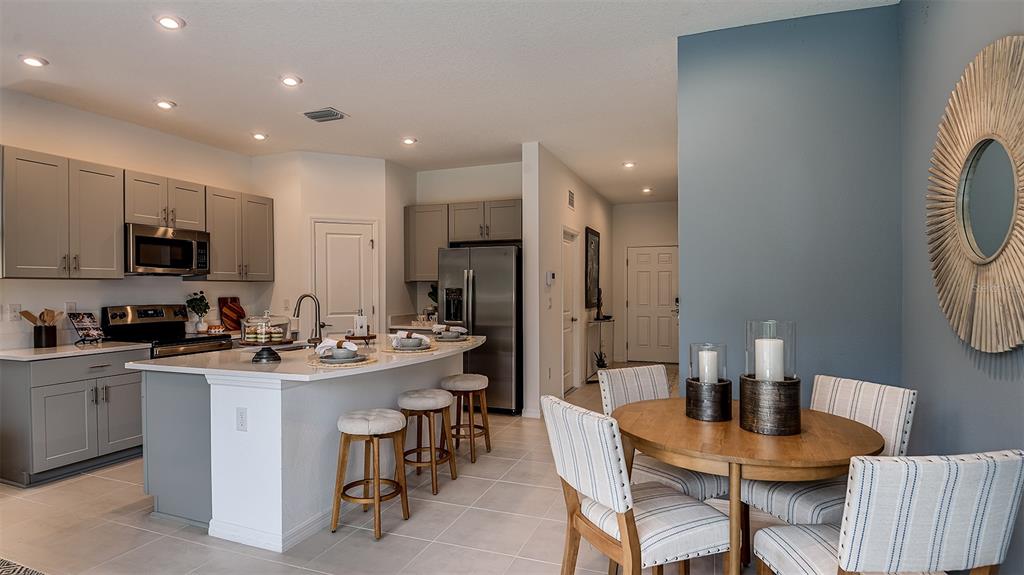 A kitchen with grey cabinets and a central island opens into a dining area — 8433 LUNAR SKYE STREET, SARASOTA, FL