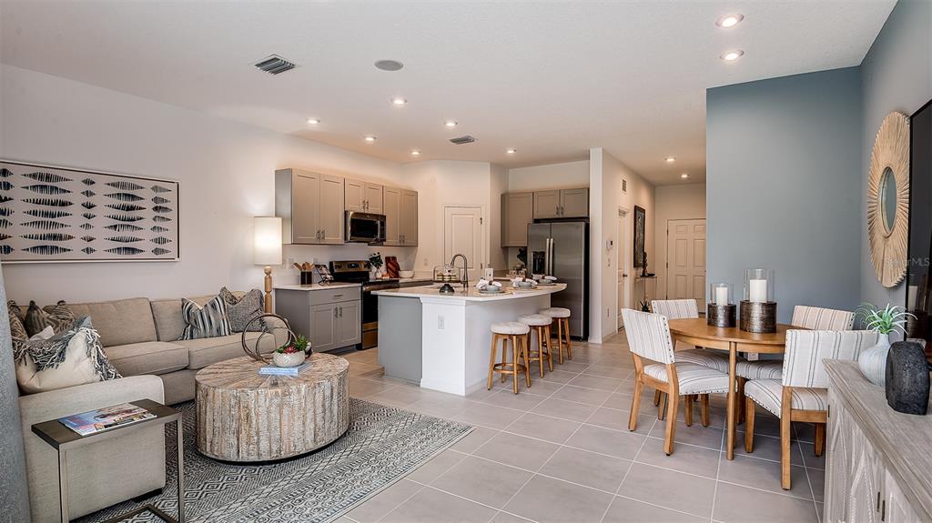 An open-concept living room and kitchen feature gray cabinetry, a central island, and dining area — 8433 LUNAR SKYE STREET, SARASOTA, FL