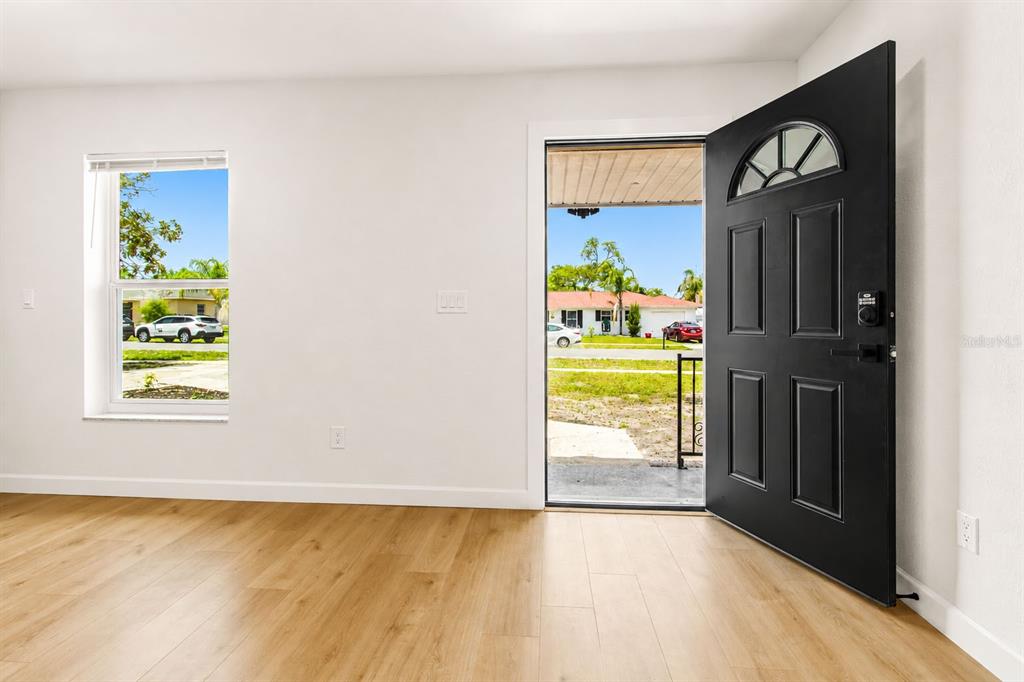 An interior view of a room with light wood flooring, a window, and an open door — 7162 CAMBRIDGE STREET, SPRING HILL, FL