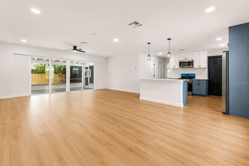 An open-concept living area with light wood flooring, a kitchen island, and sliding glass doors — 7162 CAMBRIDGE STREET, SPRING HILL, FL