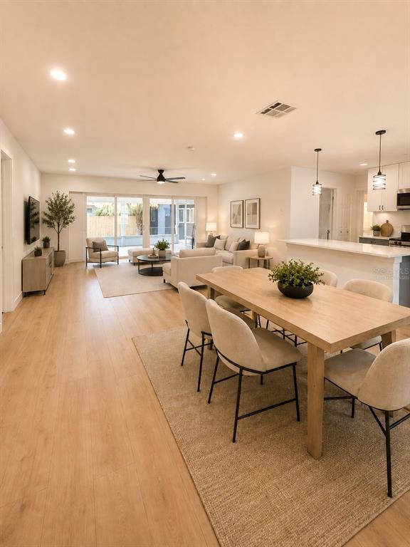 An open-concept living and dining area features light wood flooring and neutral modern furniture — 7162 CAMBRIDGE STREET, SPRING HILL, FL