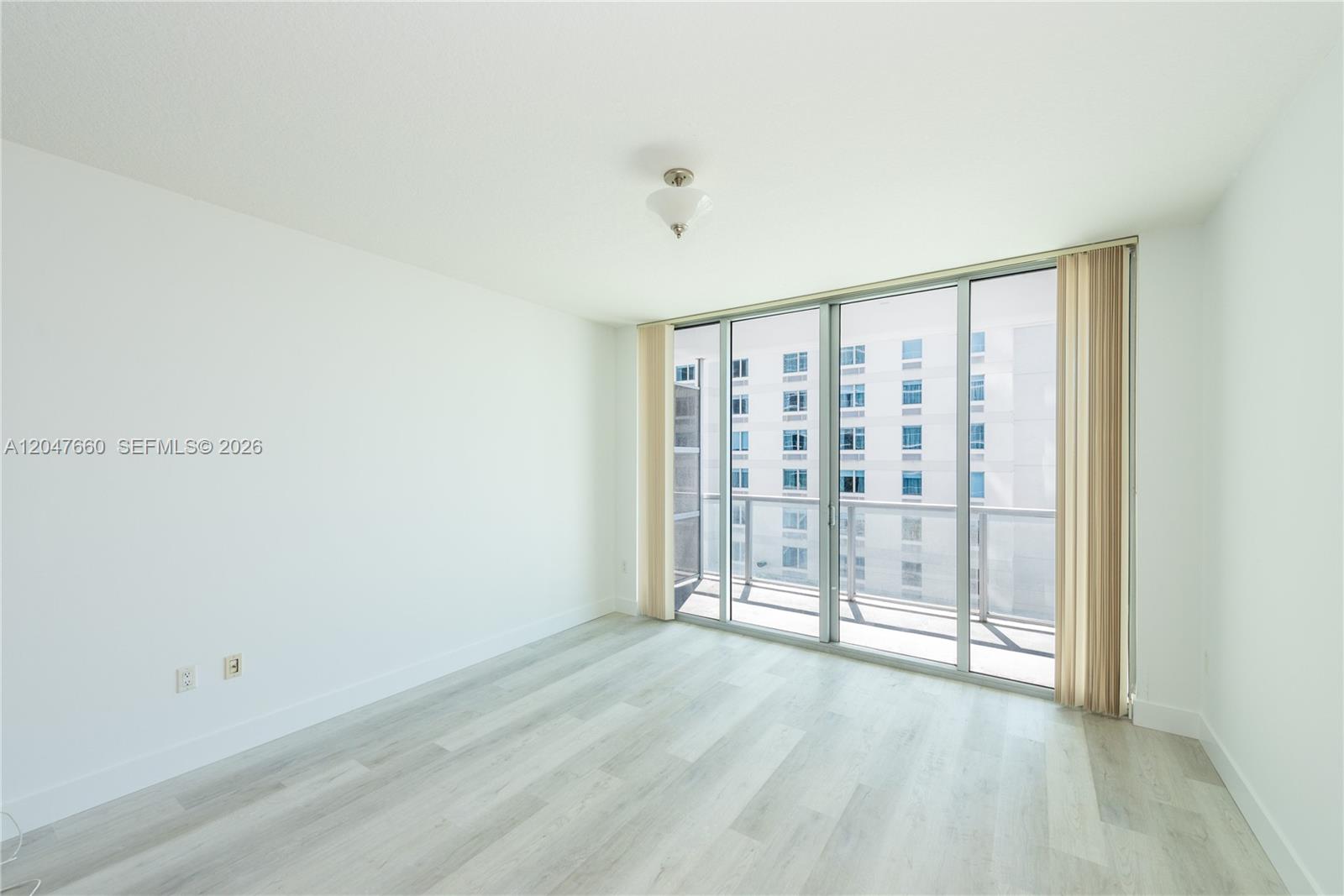 An empty room with light wood-look flooring, white walls, and a sliding glass door balcony — 79 SW 12th St, Miami FL 33130, MIAMI, FL