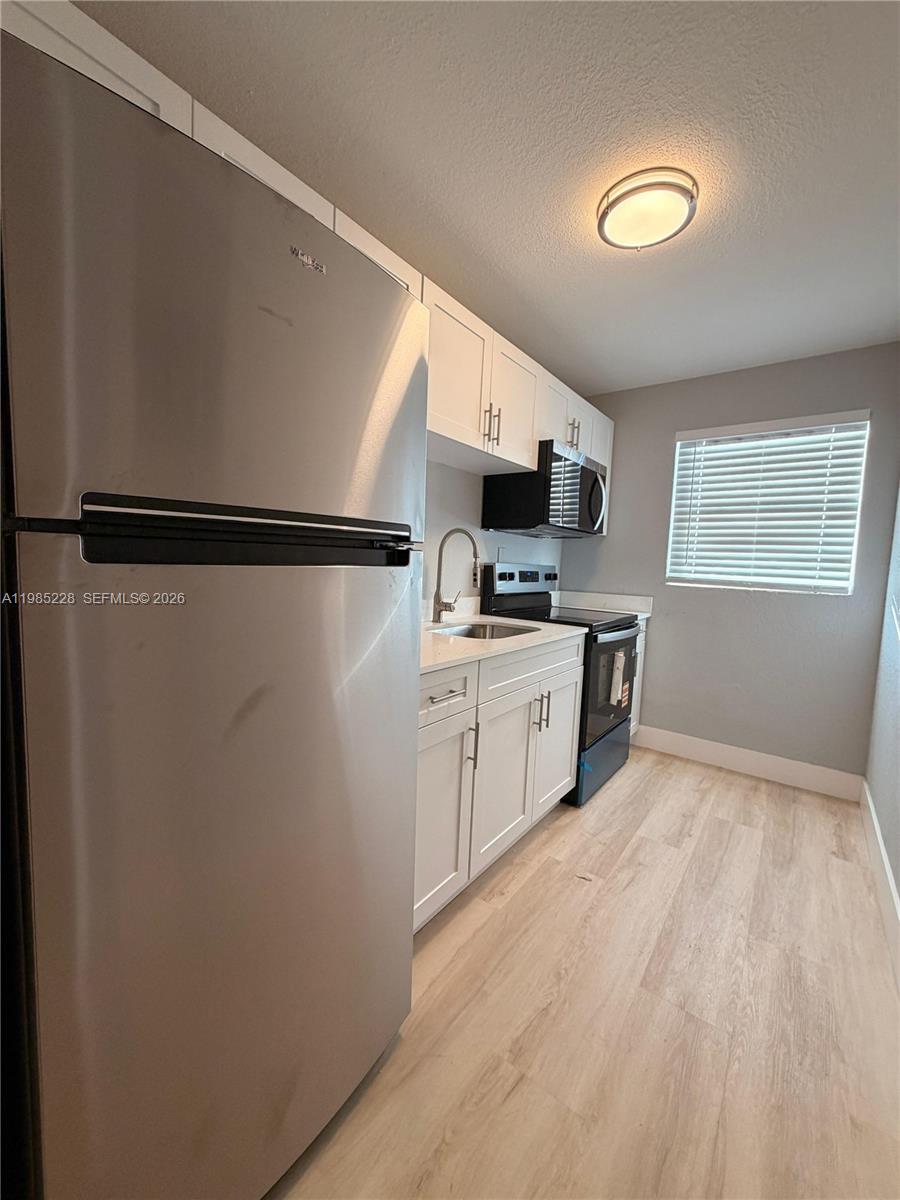 A galley kitchen features white cabinets, stainless steel appliances, and light wood-look flooring — 1258 NW 61st St # 04, Miami FL 33142, MIAMI, FL