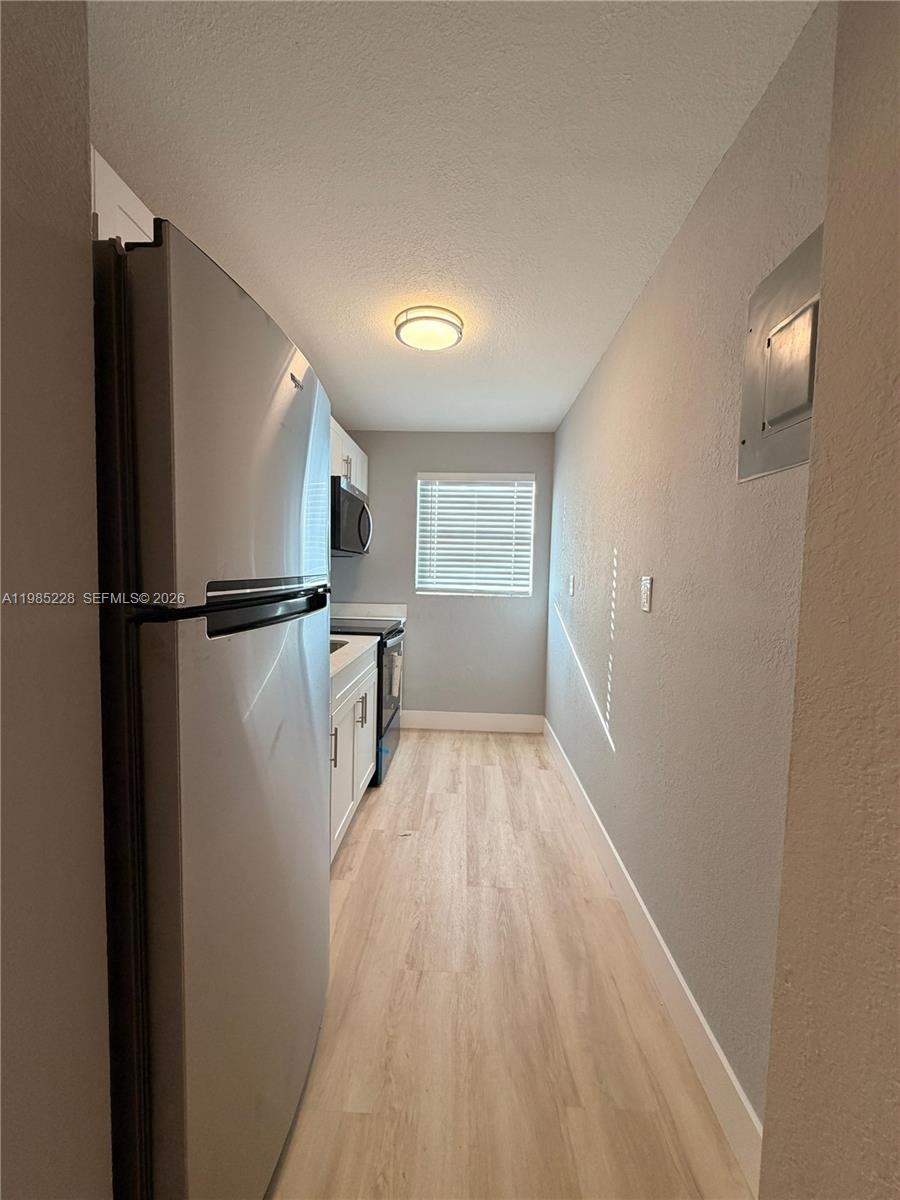 A narrow galley kitchen features stainless steel appliances, white cabinets, and light wood-look flooring — 1258 NW 61st St # 04, Miami FL 33142, MIAMI, FL