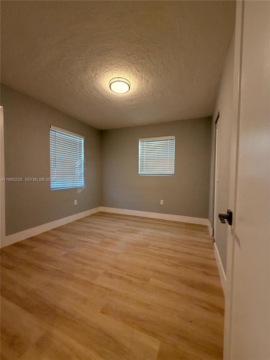 An empty bedroom features light gray walls, wood-look flooring, and two windows with blinds — 1258 NW 61st St # 04, Miami FL 33142, MIAMI, FL