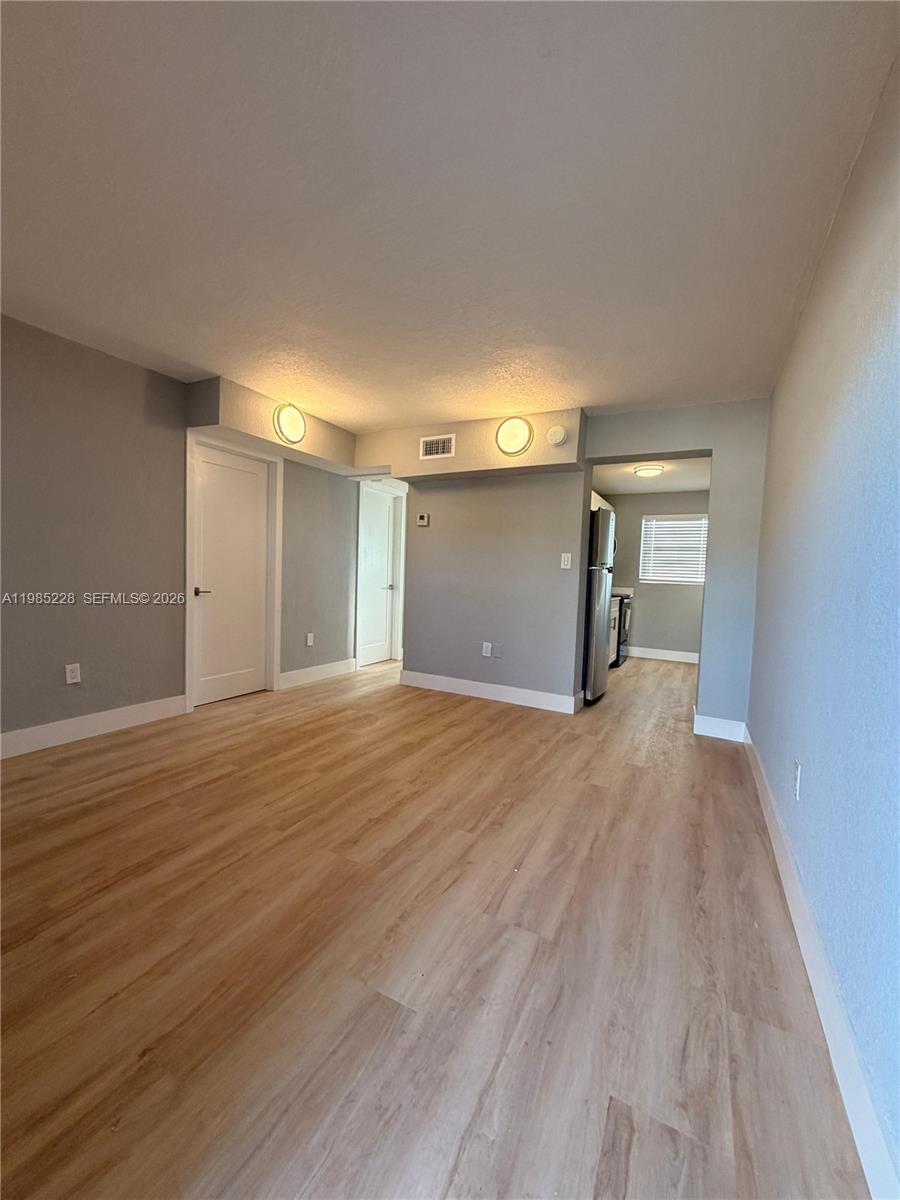 An empty room with light wood-look flooring, gray walls, and a doorway to a kitchen — 1258 NW 61st St # 04, Miami FL 33142, MIAMI, FL