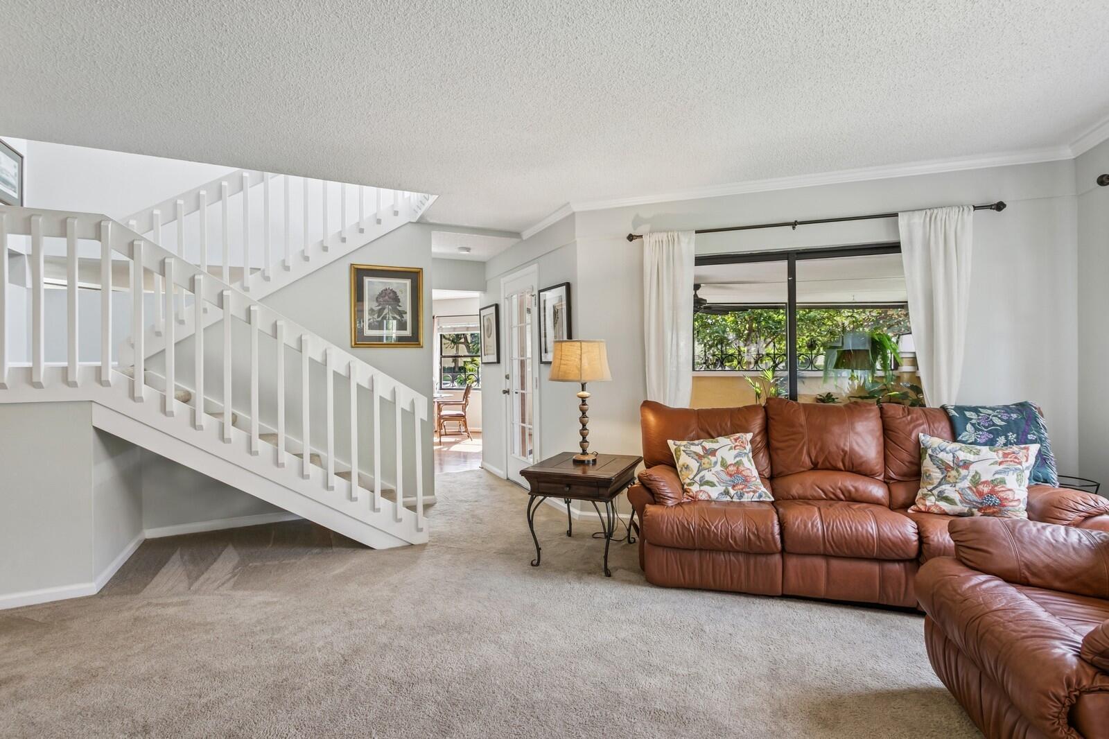 A living room features a white staircase, beige carpeting, and a brown leather sofa — 24 Uno Lago Drive, Juno Beach FL 33408, JUNO BEACH, FL