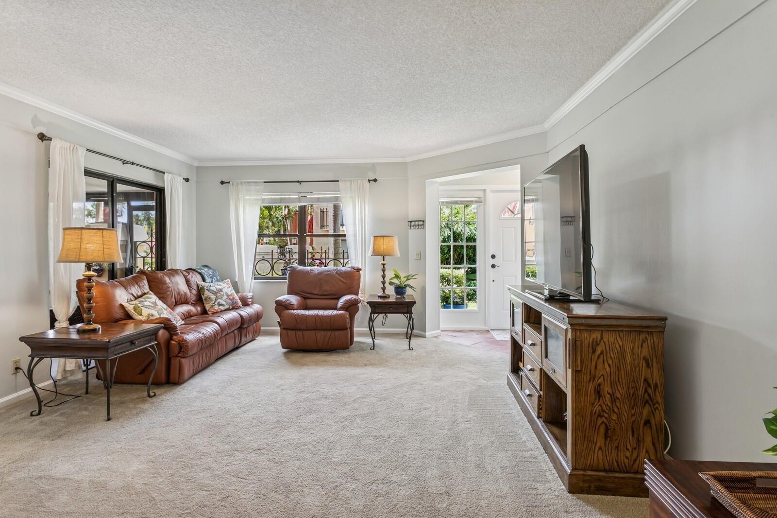 A living room features a brown leather sofa, matching recliner, television console, and carpeted floors — 24 Uno Lago Drive, Juno Beach FL 33408, JUNO BEACH, FL