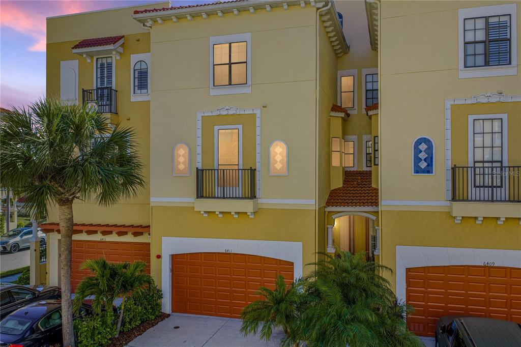 An exterior view of a yellow multi-story townhouse with orange garage doors and balconies — 6411 MAYRA SHORES LANE, APOLLO BEACH, FL