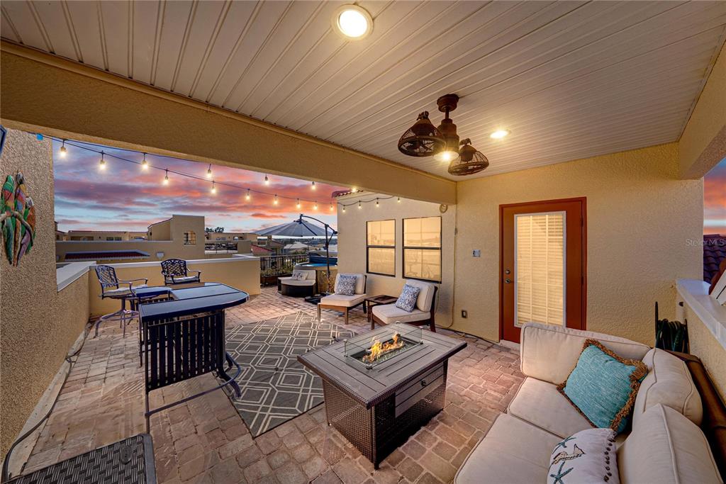 A covered rooftop patio features a fire pit, outdoor seating, and string lights at sunset — 6411 MAYRA SHORES LANE, APOLLO BEACH, FL