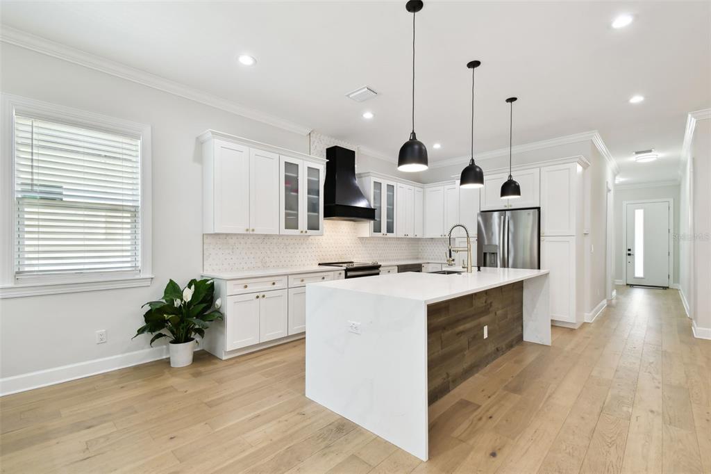A modern kitchen features white cabinetry, a large waterfall island, and wood flooring — 3106 W CHEROKEE AVENUE, TAMPA, FL