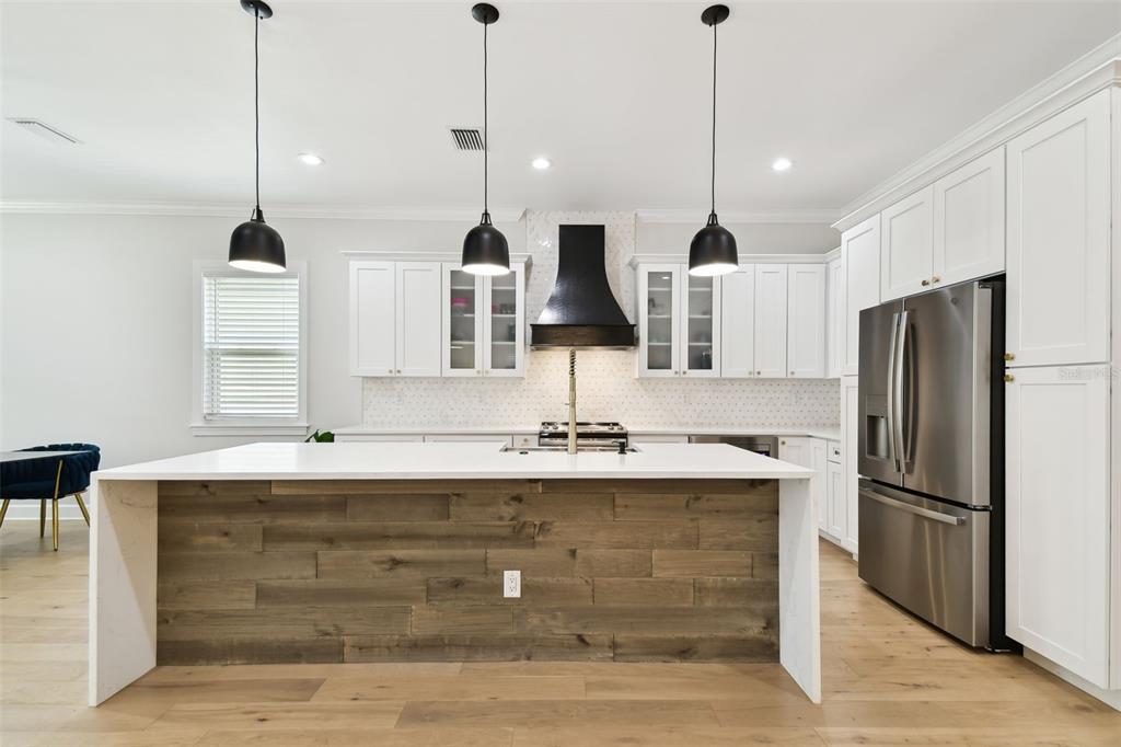 A kitchen features a wood-paneled island, white cabinetry, stainless steel appliances, and three pendant lights — 3106 W CHEROKEE AVENUE, TAMPA, FL