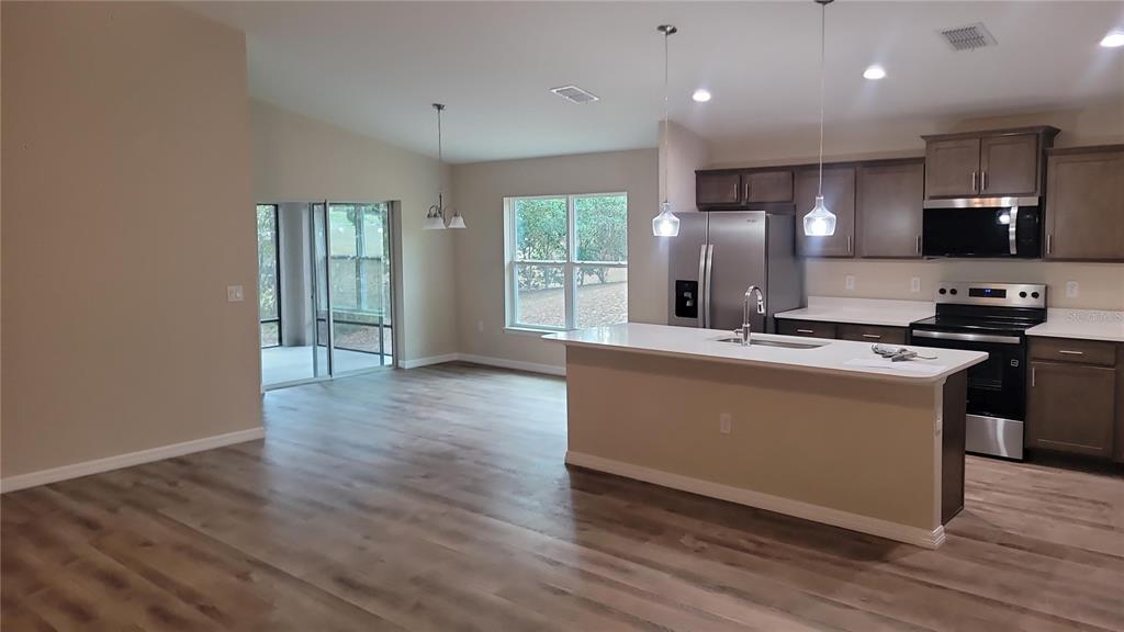 An open-concept kitchen features a white island, dark wood cabinets, and light wood-look flooring — 19396 SW 101ST PLACE ROAD, DUNNELLON, FL