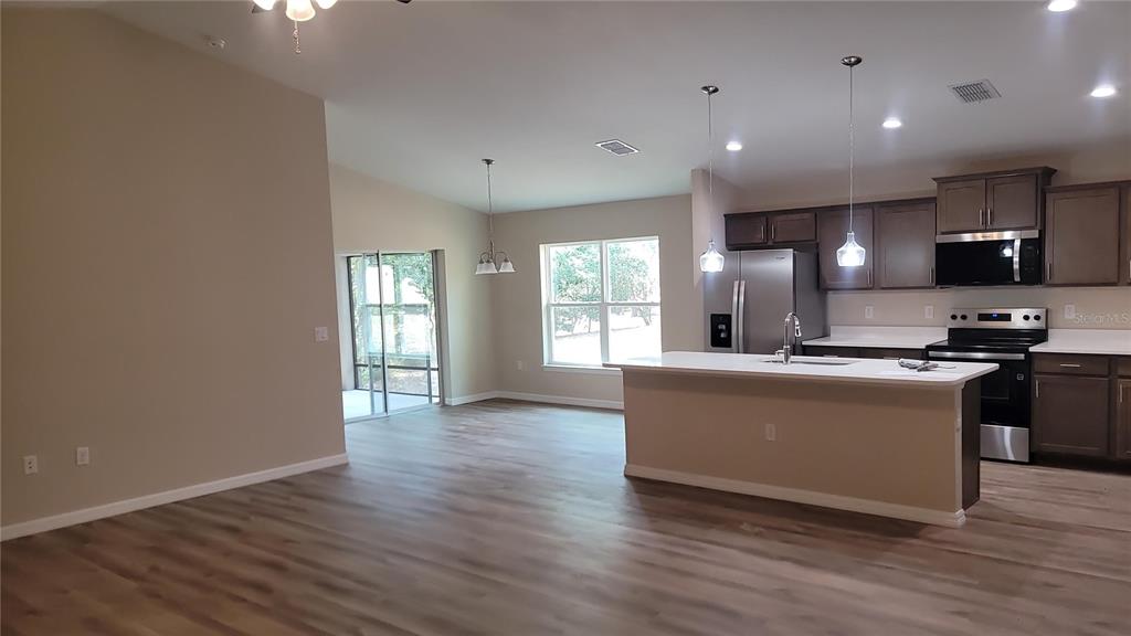 A kitchen with a center island, dark wood cabinets, and light flooring opens to a living area — 19396 SW 101ST PLACE ROAD, DUNNELLON, FL