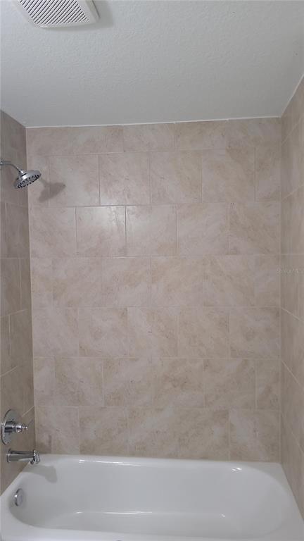 A bathroom shower and bathtub combination with beige tiled walls and a chrome showerhead — 19396 SW 101ST PLACE ROAD, DUNNELLON, FL