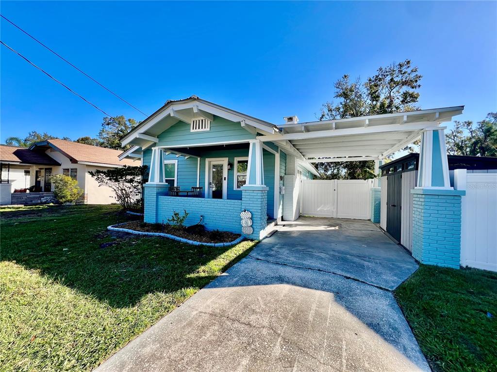 A light blue bungalow with a front porch, a carport, and a white fence — 5907 N OLA AVENUE, TAMPA, FL