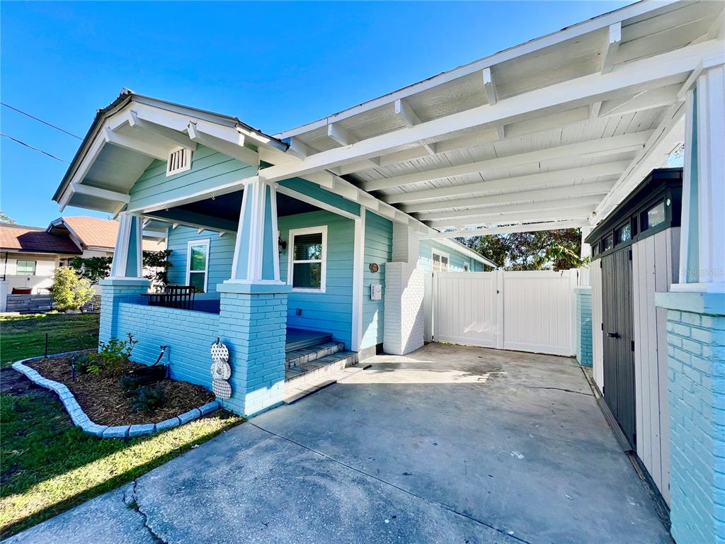 A light blue bungalow with a front porch, a concrete carport, and a white gate — 5907 N OLA AVENUE, TAMPA, FL