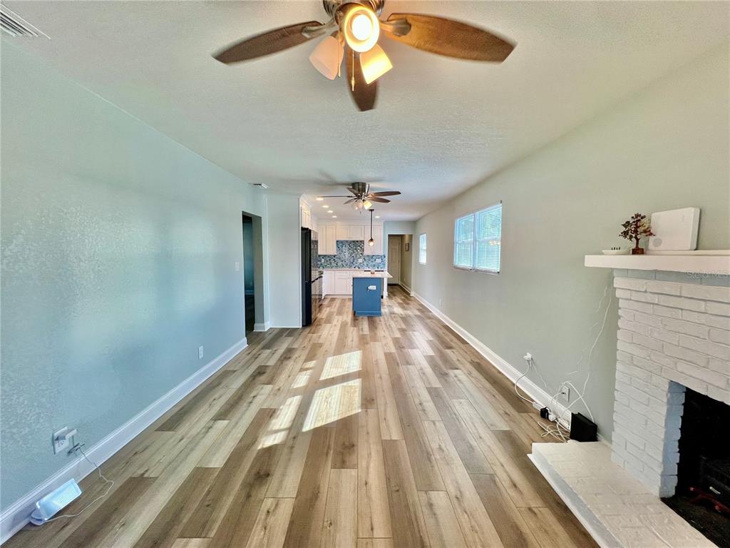 A living room with light green walls, wood-look flooring, and a white brick fireplace — 5907 N OLA AVENUE, TAMPA, FL