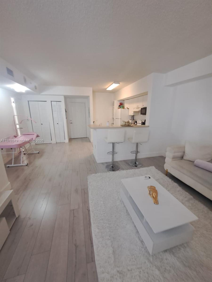 A living room with light wood floors, a white sofa, and an open kitchen area — 5077 NW 7th St # 912, Miami FL 33126, MIAMI, FL