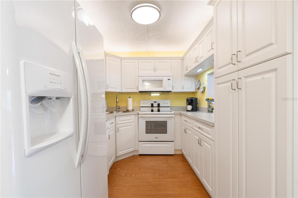 A white kitchen features white cabinets, white appliances, yellow walls, and wood-look flooring — 12218 FOX CHASE DRIVE UNIT C1, HUDSON, FL