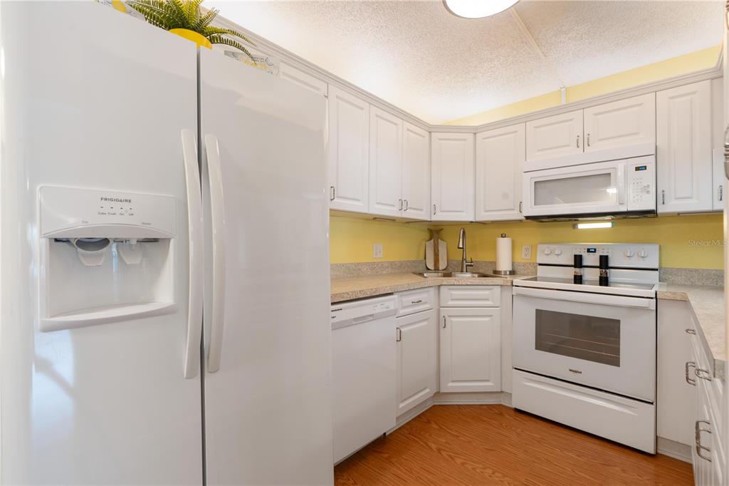 A kitchen with white cabinets, white appliances, yellow walls, and wood-look flooring — 12218 FOX CHASE DRIVE UNIT C1, HUDSON, FL