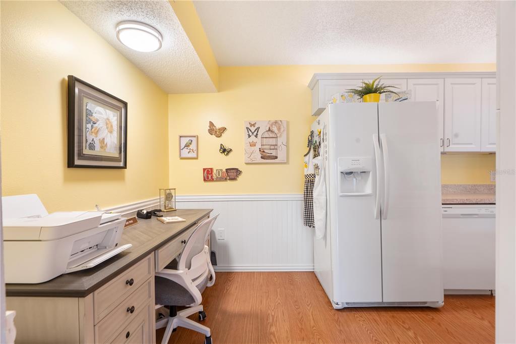 A kitchen area features a desk workspace, yellow walls, white wainscoting, and a white refrigerator — 12218 FOX CHASE DRIVE UNIT C1, HUDSON, FL