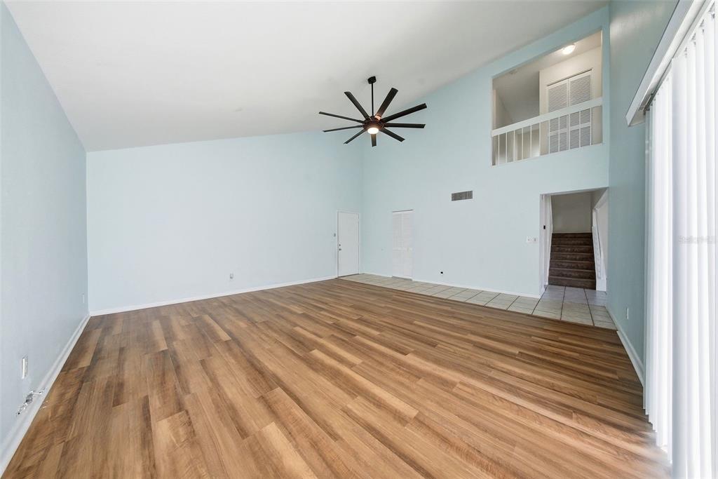 A spacious living room features light blue walls, wood-look flooring, and a high vaulted ceiling — 2617 BARKSDALE COURT, CLEARWATER, FL