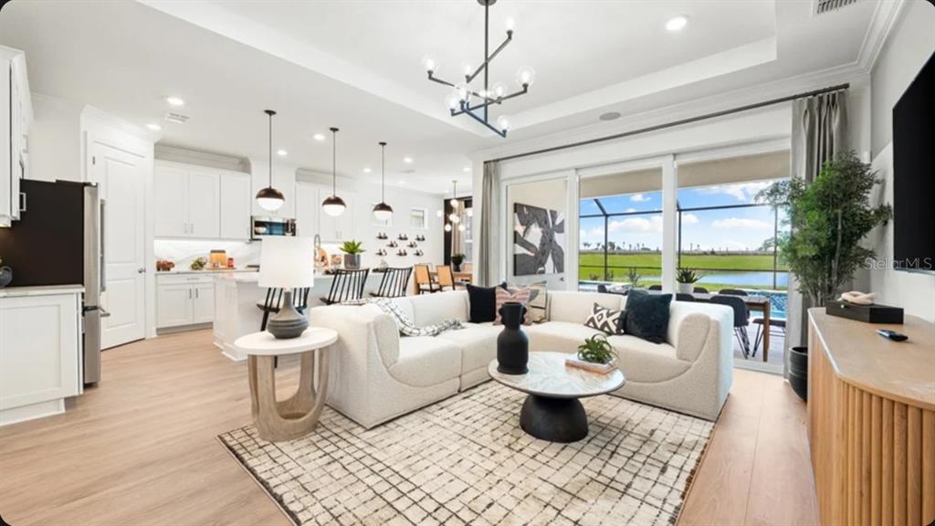 A modern open-concept living room and kitchen feature white cabinetry, light wood flooring, and sliding doors — 7649 MOONBEAM AVENUE, SARASOTA, FL
