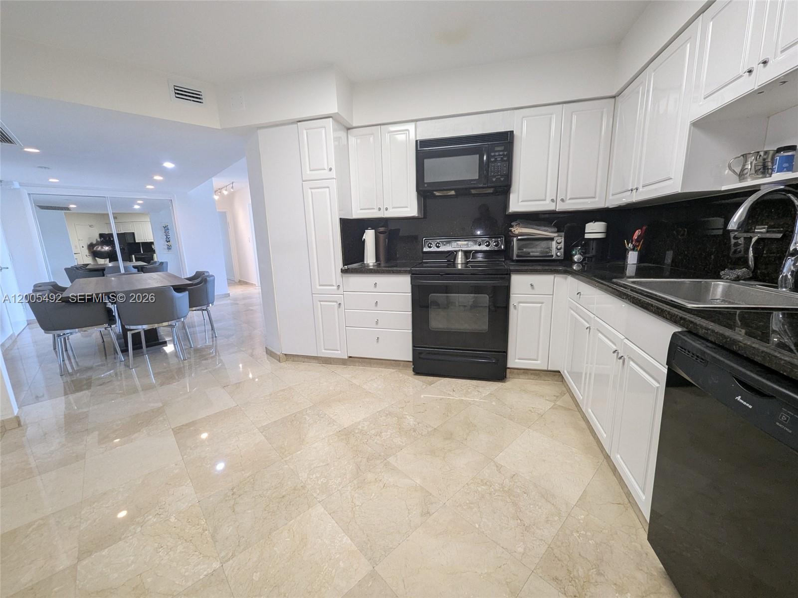 A kitchen features white cabinets, black appliances, dark countertops, and light-colored tile flooring — 5161 Collins Ave # 518, Miami Beach FL 33140, MIAMI BEACH, FL