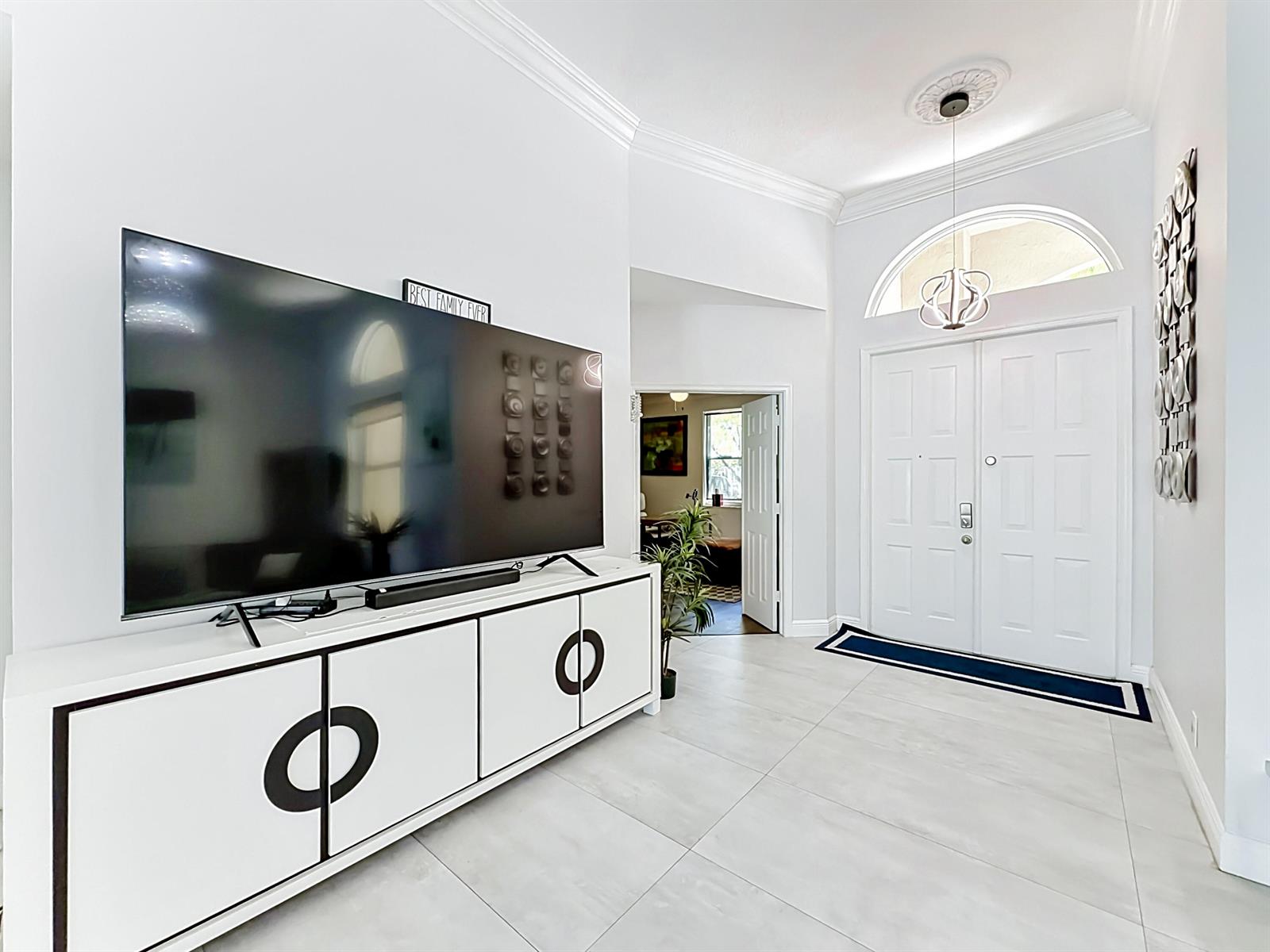 A bright entryway features white tile floors, a large television console, and double front doors — 3836 Heron Ridge Lane, Weston FL 33331, WESTON, FL
