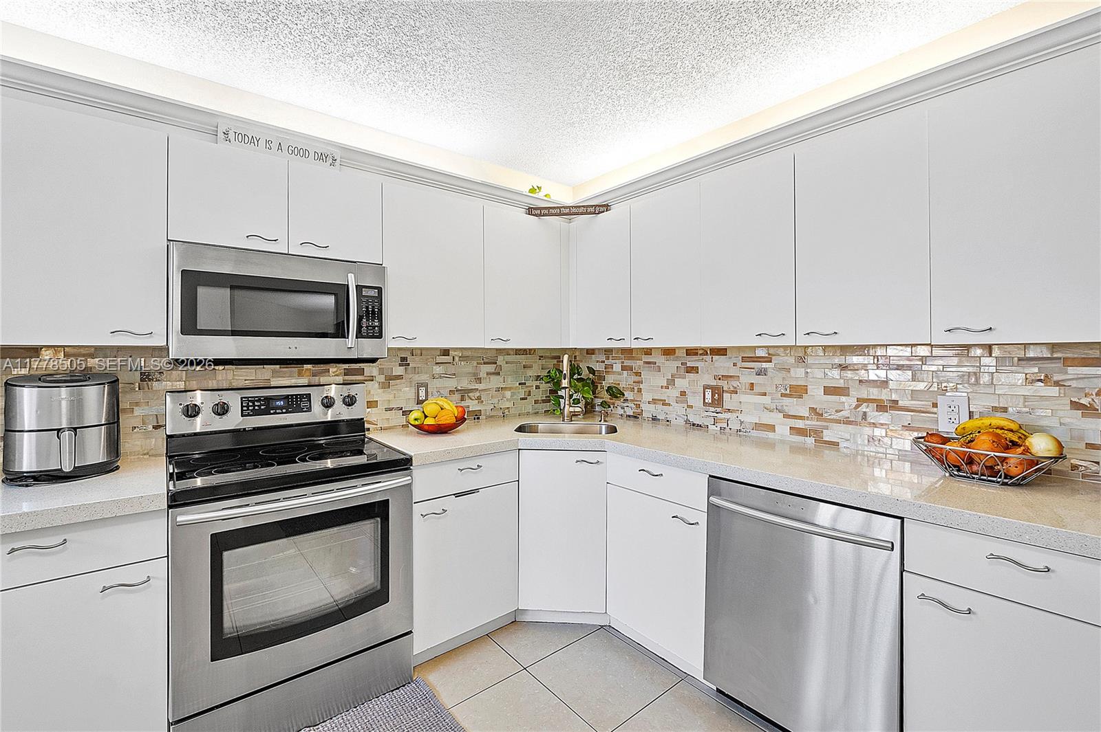 A kitchen features white cabinets, stainless steel appliances, a tiled backsplash, and light-colored floor tiles — 4101 E Coral Tree Cir # 313, Coconut Creek FL 33073, COCONUT CREEK, FL