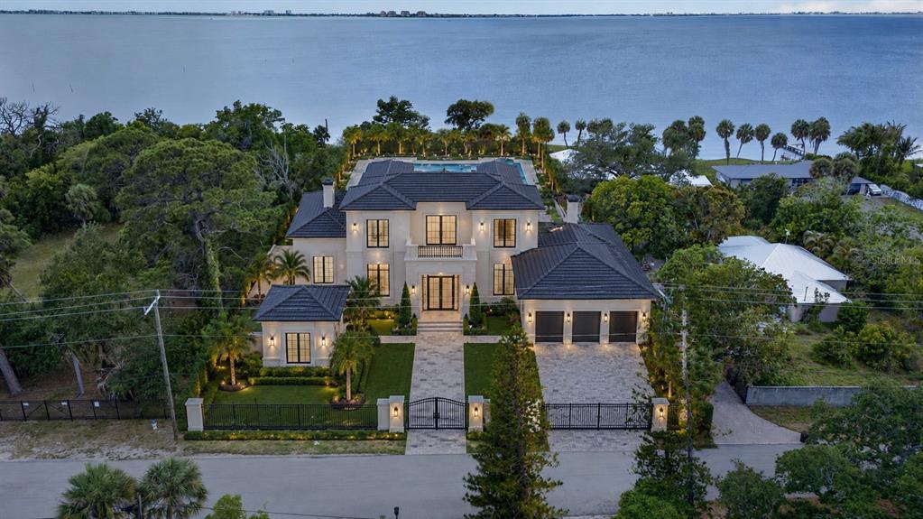 An aerial view of a two-story waterfront mansion with a tiled roof and gated driveway — 8258 LONGBAY BLVD, SARASOTA, FL